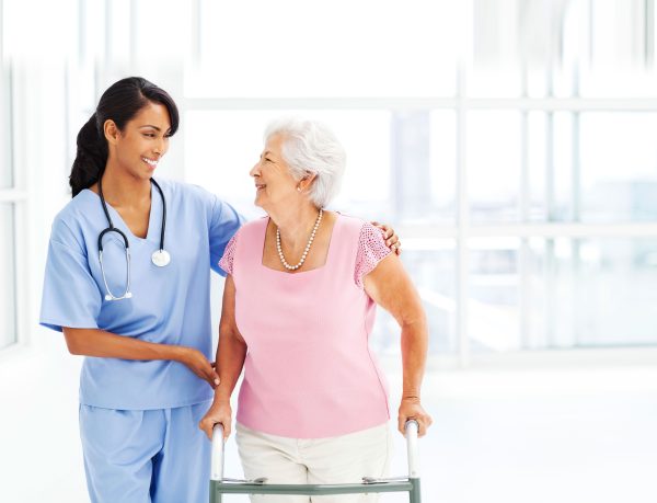 Physician assisting an elderly patient walk down a hall