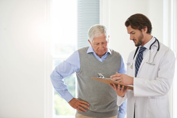 Physician with clipboard speaking to older male patient