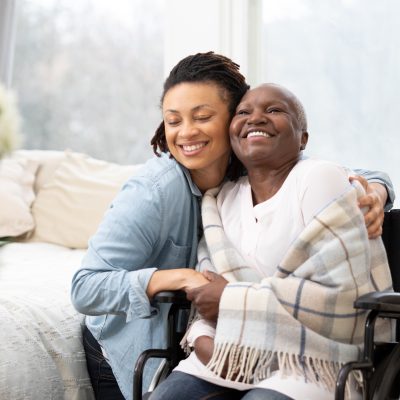 Young woman hugs senior woman in wheelchair