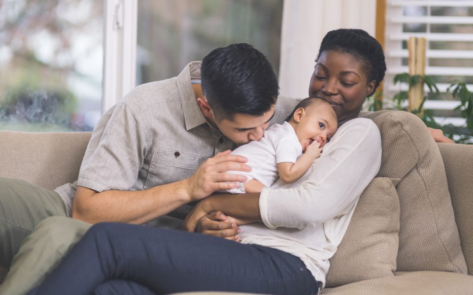 couple snuggle with their infant daughter on the couch in their living room