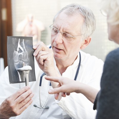 Mature doctor presenting x-ray and knee arthroplasty to female patient
