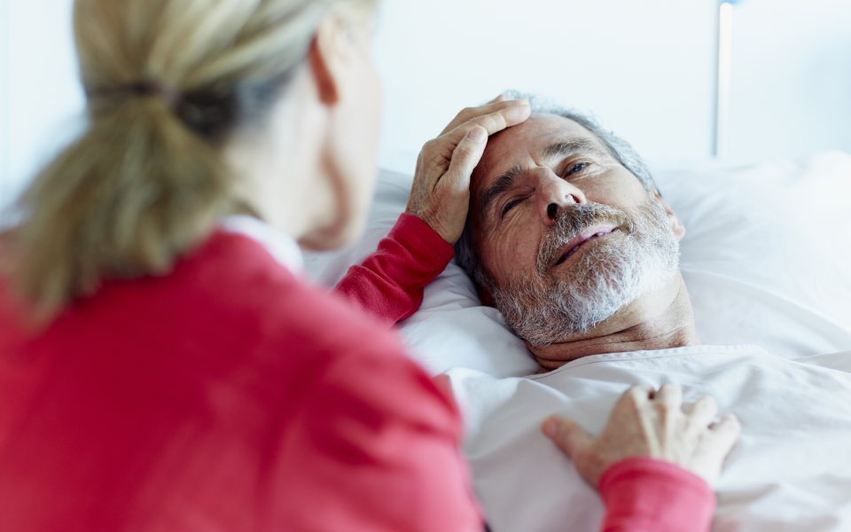 Male patient in hospital bed being comforted by wife