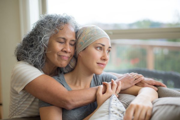 Young woman in cancer treatment being embraced by her mother.