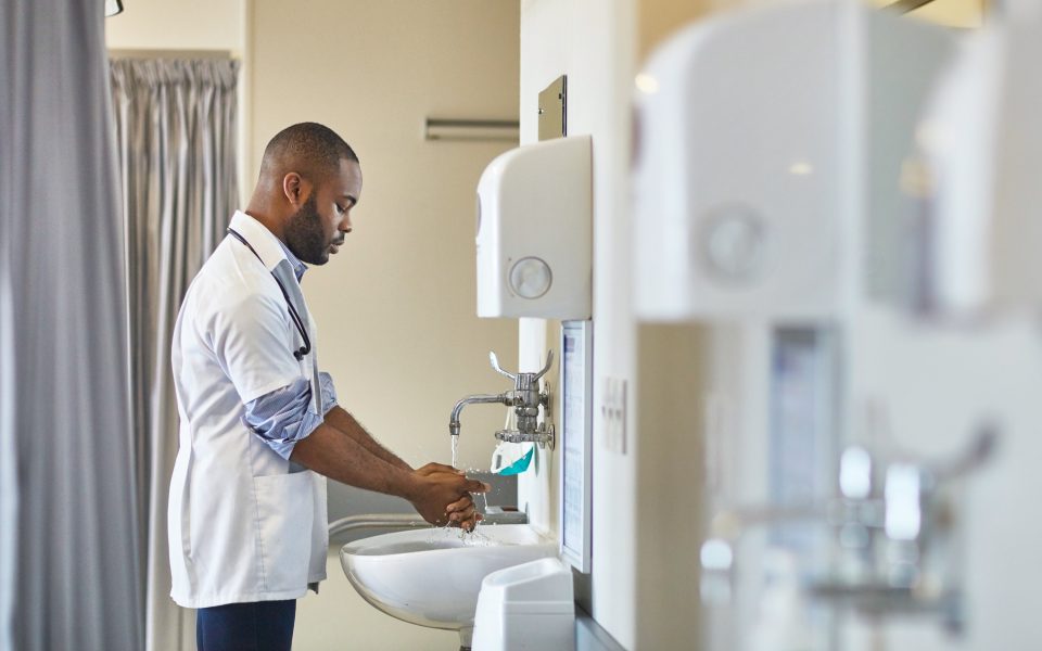 Young male doctor washing hands at sink