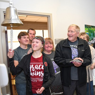 Young female cancer patient ringing the bell to signal the end of her cancer treatment
