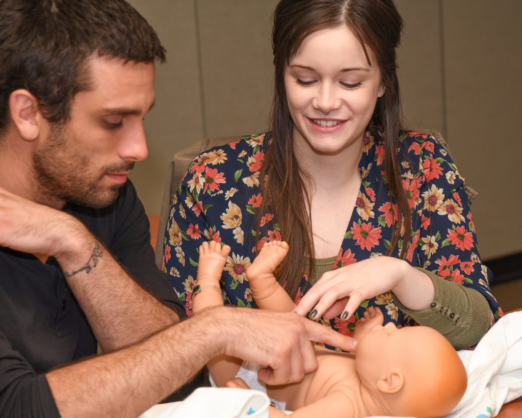 Man and woman practice diapering a baby doll